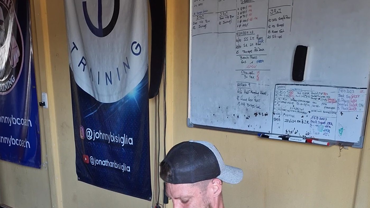 Los banners de JB Training en la pared amarilla del estudio y la pizarra con rutinas